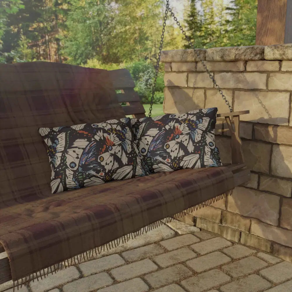 Outdoor lounge space with butterfly-patterned pillows and a plaid blanket on a wooden porch swing